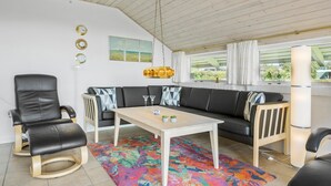 A modern living room with a black leather sofa, a wooden coffee table, and a colorful rug. There are two black leather chairs, a white floor lamp, and a hanging light fixture. - 3 bedroom nice home in Egernsund (Egernsund)