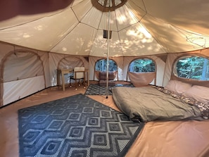Relax in a spacious tent with a comfortable bed, seating area, and large window offering a forest view.