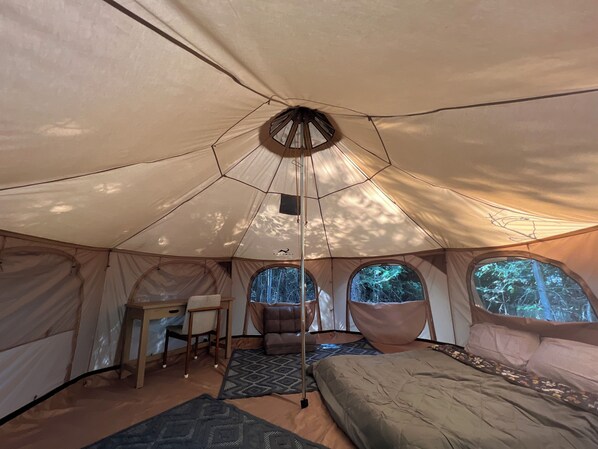 Cozy sleeping area with a bed, desk, and chair, offering a view of the surrounding forest through a circular window.