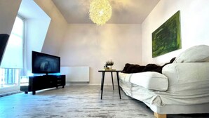 Una sala de estar moderna con un televisor de pantalla plana, un sofá blanco, una mesita y una lámpara de araña original.