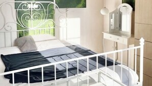 Un dormitorio con una estructura de cama metálica blanca, una mesita de noche con lámpara y dos cuadros abstractos verdes en la pared.
