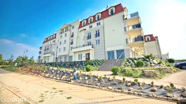 Un edificio residencial de varios pisos con balcones, un jardín ajardinado y un camino pavimentado.