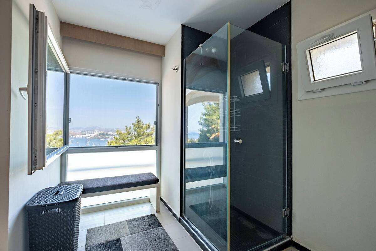 A modern bathroom with a glass shower door, a bench by the window, and a view of the outdoors.