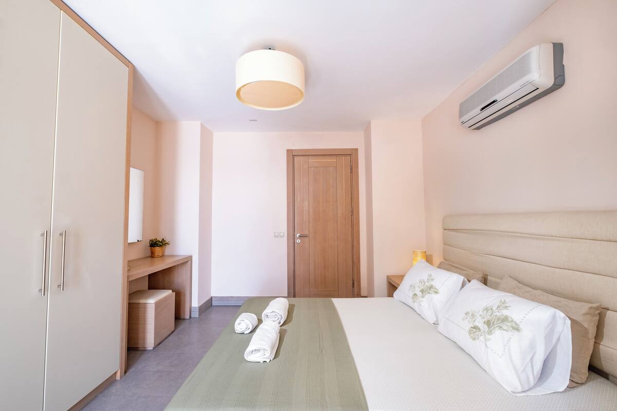 A hotel room with a bed, a wardrobe, a bedside table with a lamp, and an air conditioning unit on the wall.