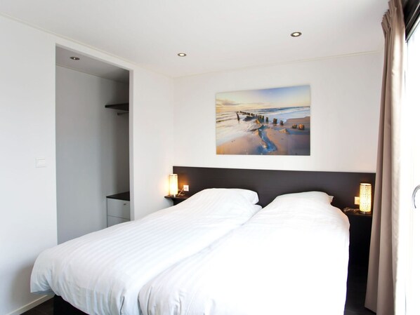 Une chambre à coucher avec un grand lit, un tableau représentant une scène de plage et deux lampes de chevet.