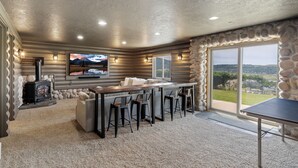 A cozy living room with a fireplace, a TV, a stone accent wall, and a large window offering a scenic view.