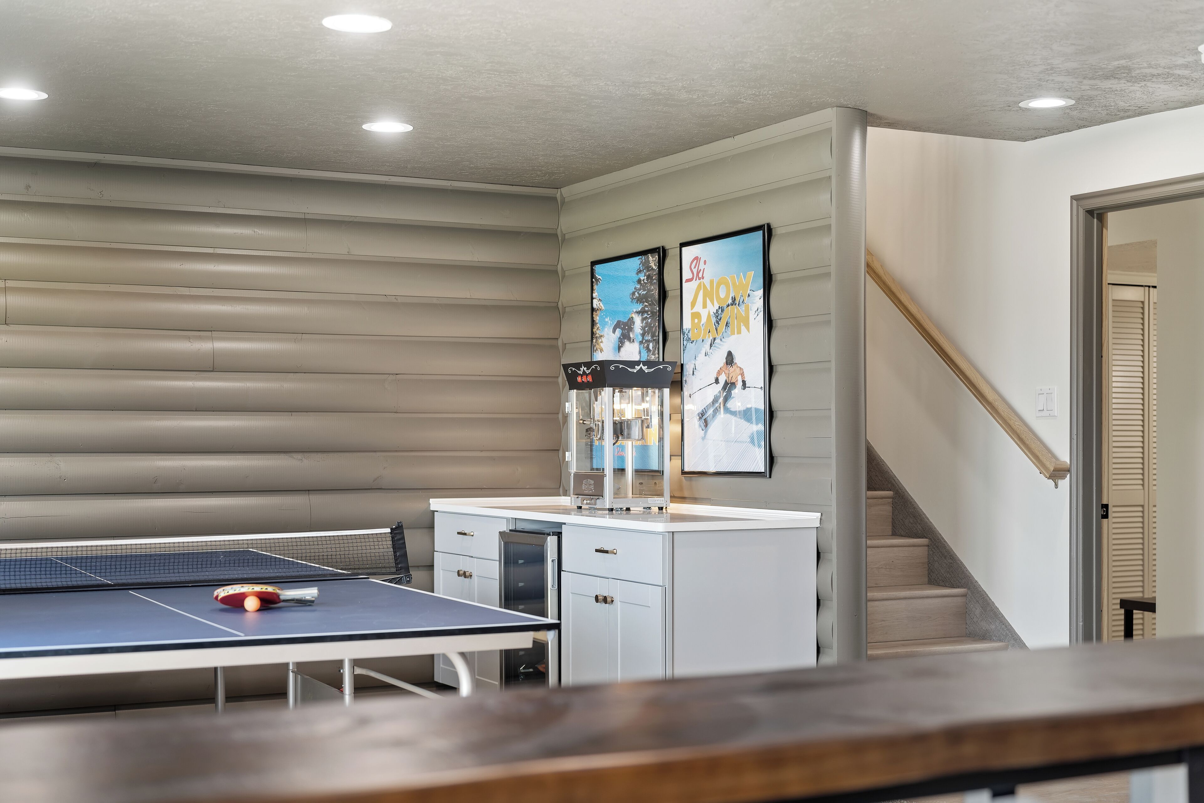Una mesa de ping pong en una habitación con una zona de cocina y una escalera.