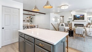 A modern kitchen with a large island, pendant lighting, and a fireplace in the living area.