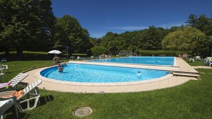 A rectangular swimming pool with a tiled deck surrounding it, set in a grassy area with trees in the background. - Riva del Caolino in Ispra (Ispra)