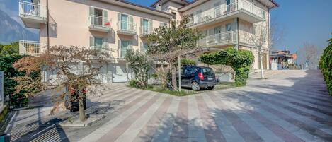 A multi-story residential building with balconies, a paved driveway, and a parked car.