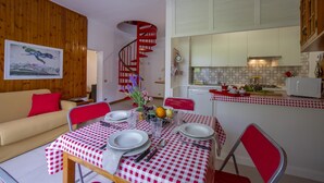 A dining area with a checkered tablecloth, a red spiral staircase, and a kitchen with white cabinets. - Rododendro Rosso in Ispra (Ispra)