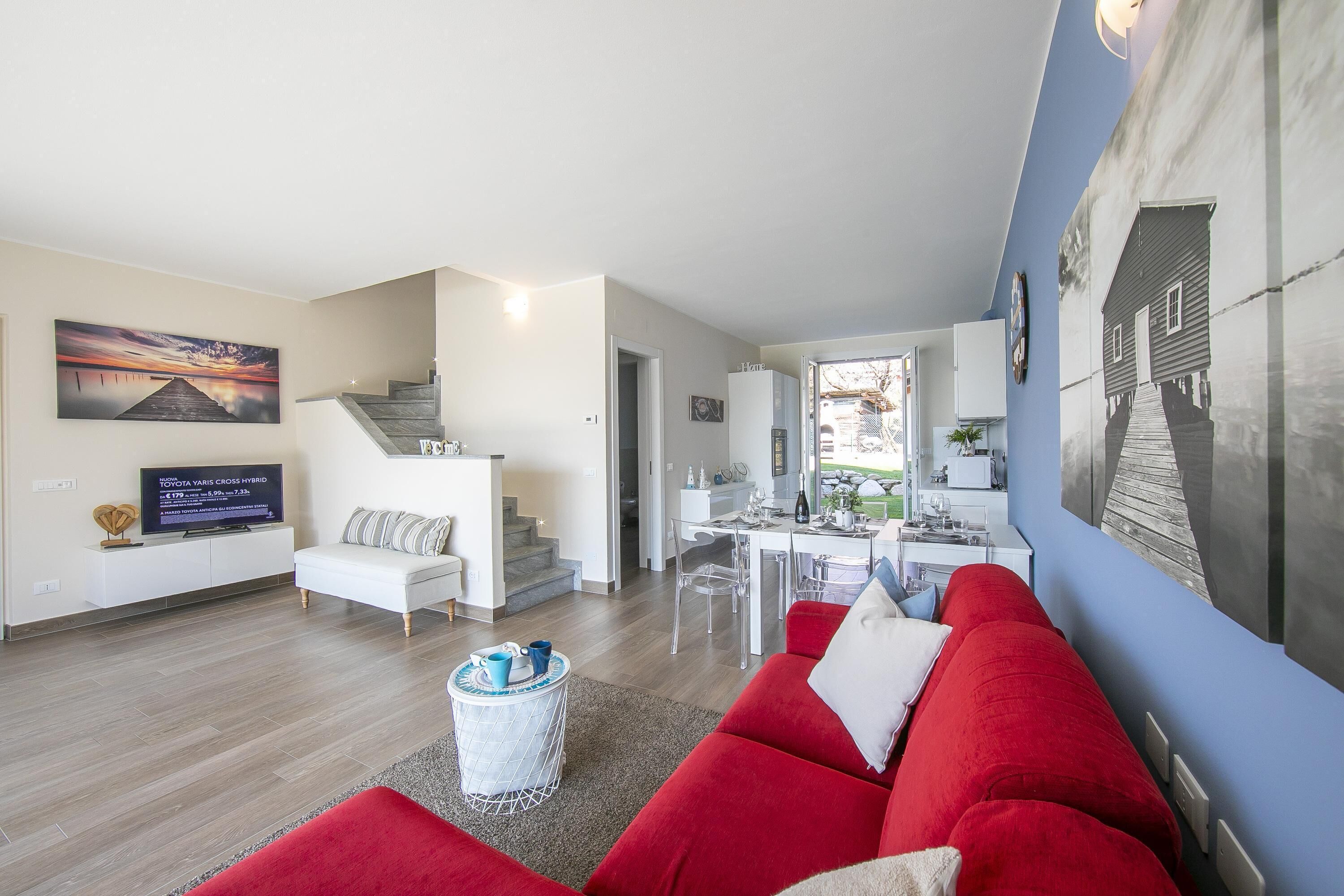 Ein modernes Wohnzimmer mit einem roten Sofa, einem Fernseher und einer Essecke mit Tisch und Stühlen.