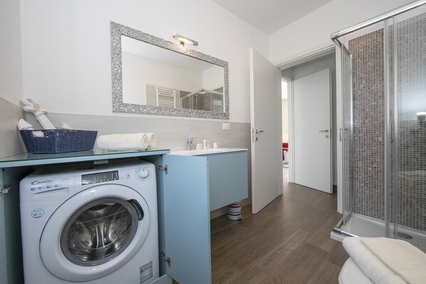 Une salle de bain moderne équipée d’un lave-linge, d’un évier, d’un miroir et d’un espace douche.