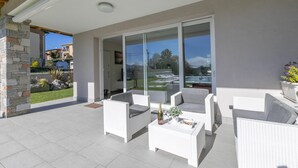 Eine überdachte Terrasse mit weißen Korbmöbeln, eine Glastür zum Pool und eine Stein Säule.