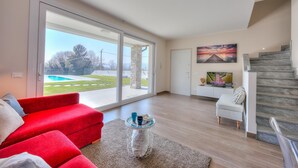 Ein geräumiges Wohnzimmer mit einem roten Sofa, einem Couchtisch und Blick auf einen Swimmingpool durch große Glasschiebetüren.