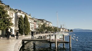A waterfront promenade with buildings, a dock, and boats. - Vicolo 42 At 200m From Lake (Salò)