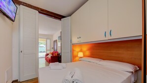 A hotel room with a bed, white towels, a wooden headboard, and a TV on the wall. - Vicolo 42 At 200m From Lake (Salò)