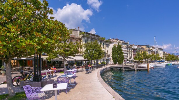 A waterfront café with outdoor seating, a dock, and boats in the background. - Vicolo 42 At 200m From Lake (Salò)