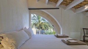 A bedroom with a large arched window, a bed with white linens, and a view of palm trees outside. - Villa Pruno in Scicli (Scicli)