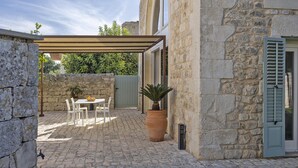 A stone building with a covered patio, a table with chairs, and a potted plant. - Villa Pruno in Scicli (Scicli)