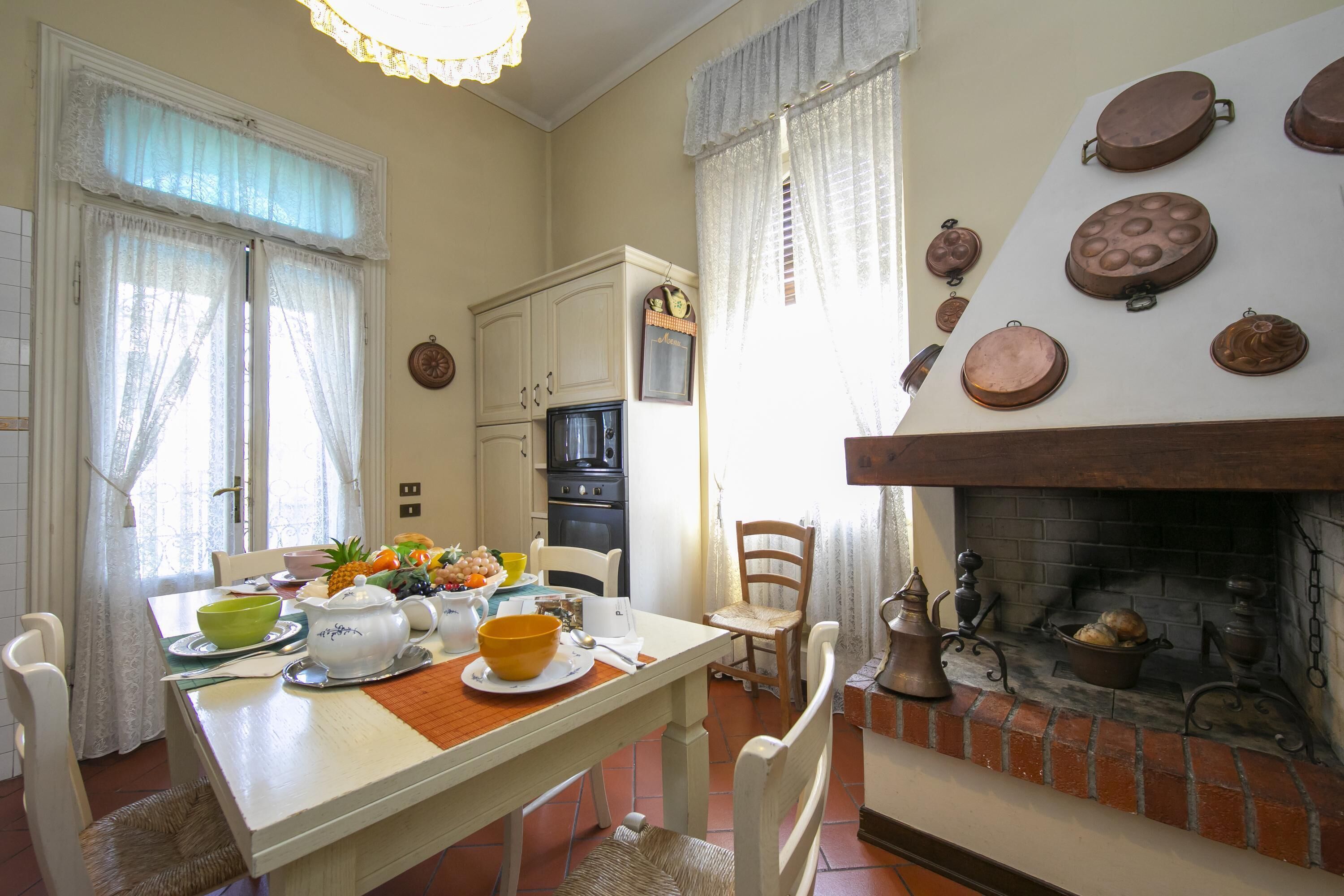 A dining area with a table set for breakfast, a fireplace with decorative plates, and a kitchen in the background.