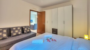 A hotel room with a bed, a sofa, a wardrobe, and a nightstand with a lamp. - Va Pensiero sul Lago Stunning View (Tronzano Lago Maggiore)