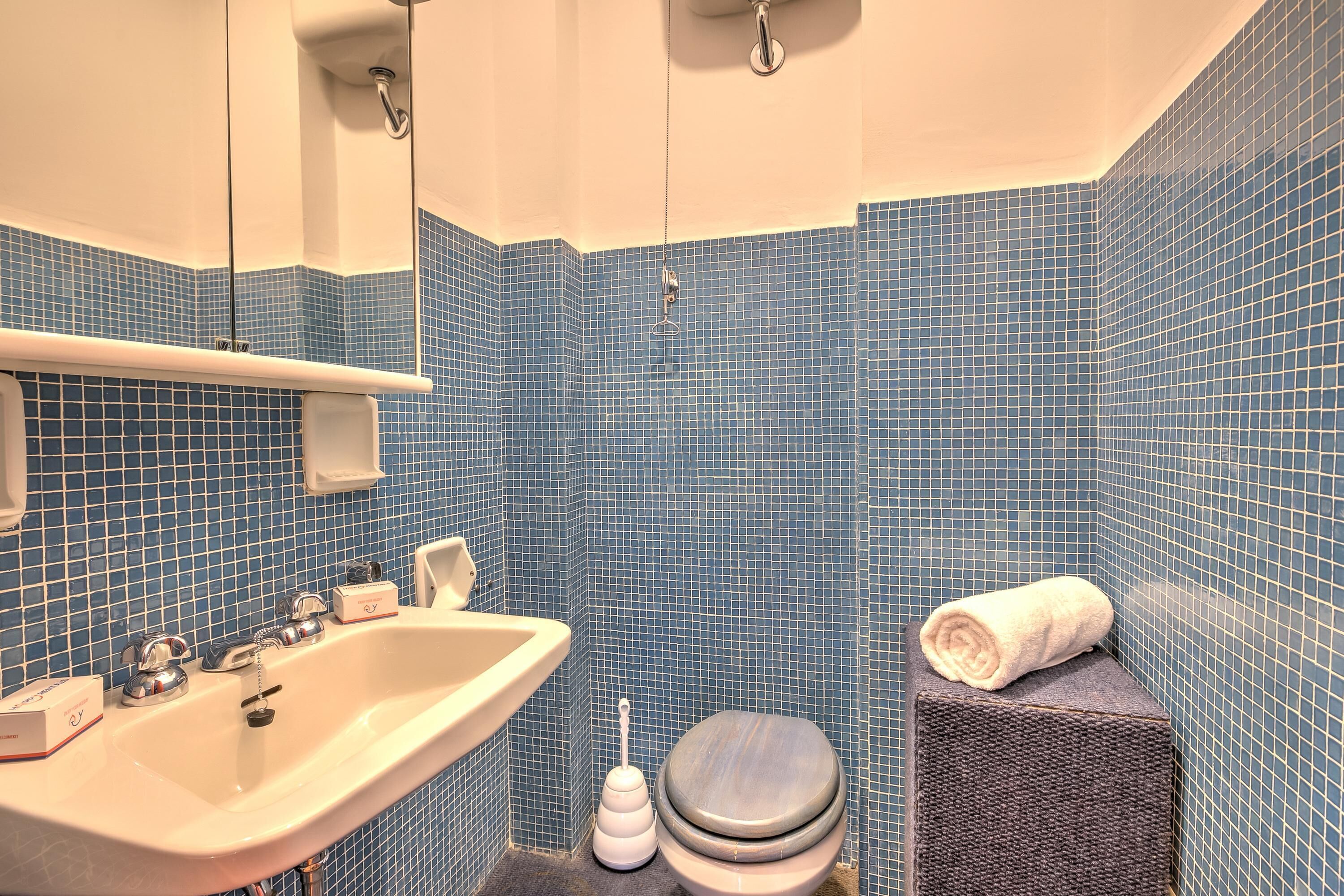 A bathroom with a white sink, a toilet, and a towel on a stool.