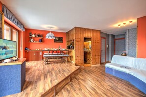Un salon chaleureux avec un banc en bois, un canapé, un téléviseur et un coin cuisine doté d’un bar.
