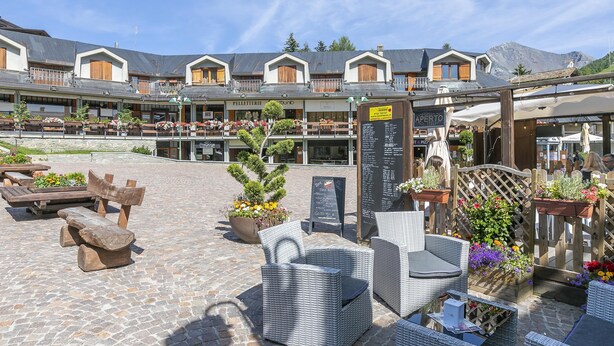 A courtyard with outdoor seating, a menu board, and a sign for 'APERTO'. - Terrazza Dei Principi Few Steps From Ski (Sestriere)