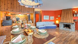 A cozy dining area with a wooden table set for four, a fireplace, and a kitchen in the background. - Terrazza Dei Principi Few Steps From Ski (Sestriere)