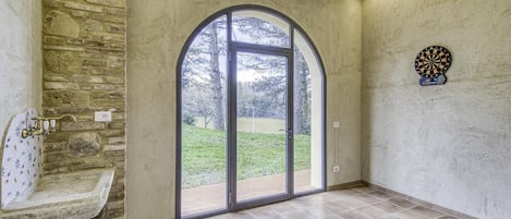 Ein Zimmer mit Steinwand, einem großen Bogenfenster, einer Dartscheibe und einem Waschbecken mit Steintischplatte.