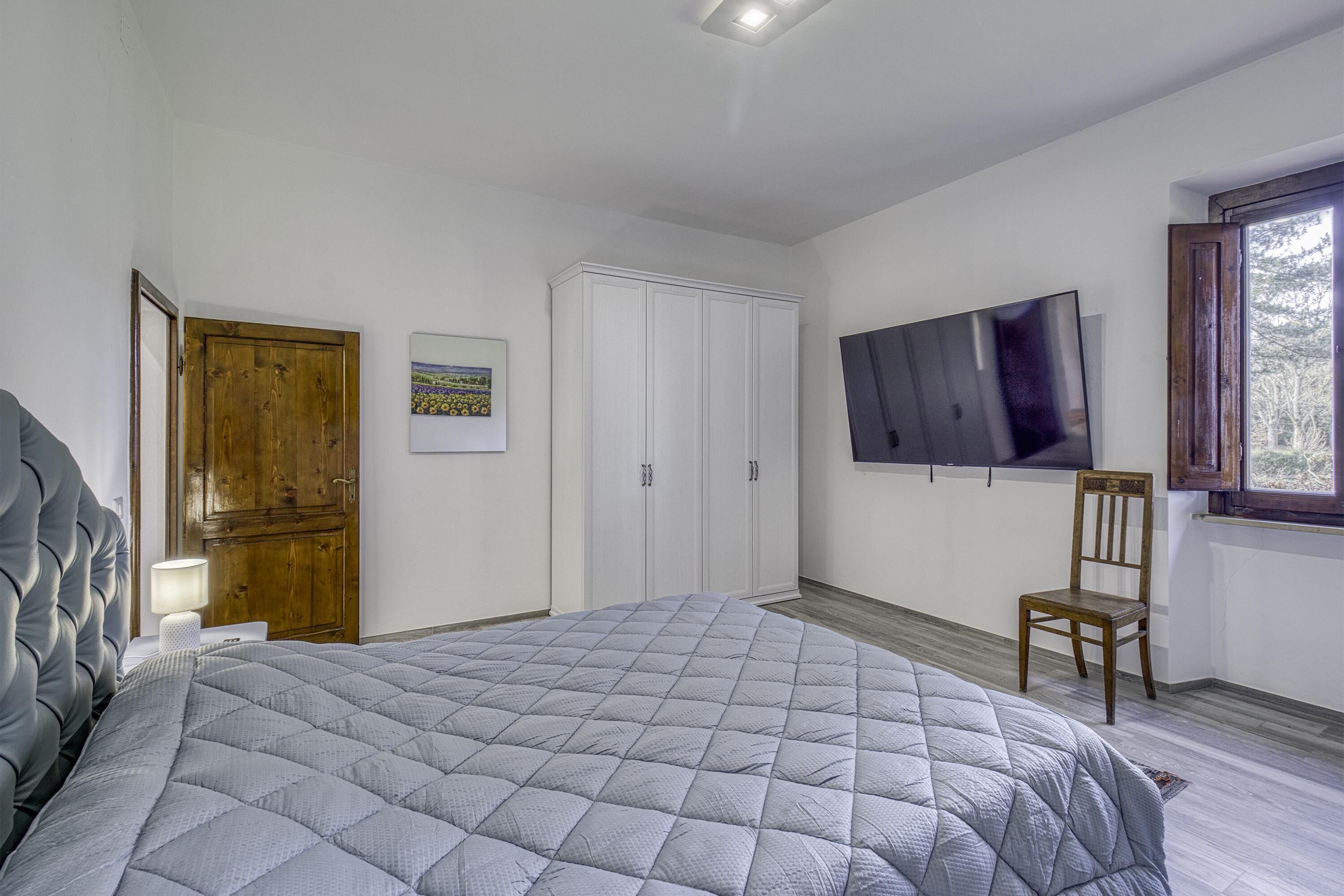 Une chambre avec un grand lit, une porte en bois, une armoire, un téléviseur et une fenêtre.