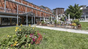 A modern building with a wooden facade and a covered outdoor seating area with sunflowers and flowers. - Sestriere Terrace Apt Few Steps From Ski (Sestriere)