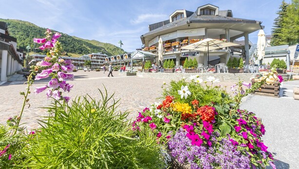 A hotel with a covered outdoor area, a flower garden, and a mountainous backdrop. - Sestriere Terrace Apt Few Steps From Ski (Sestriere)
