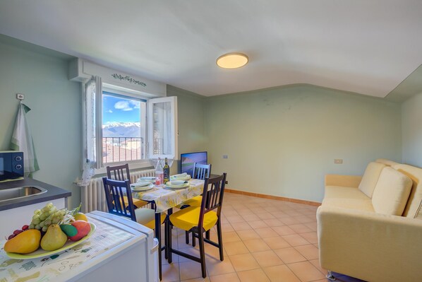 Un coin repas avec une table dressée pour deux personnes, un canapé et une vue sur les montagnes par la fenêtre.