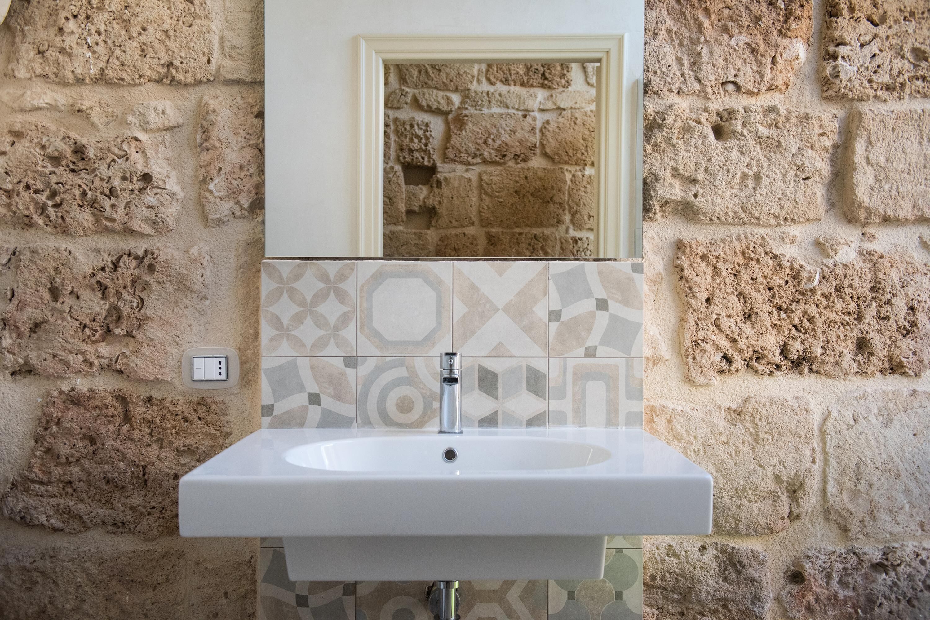 Un baño con un lavamanos blanco, un espejo encima y una pared de piedra.
