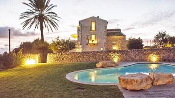 Un edificio in pietra con piscina, immerso in un prato curato e con una palma.