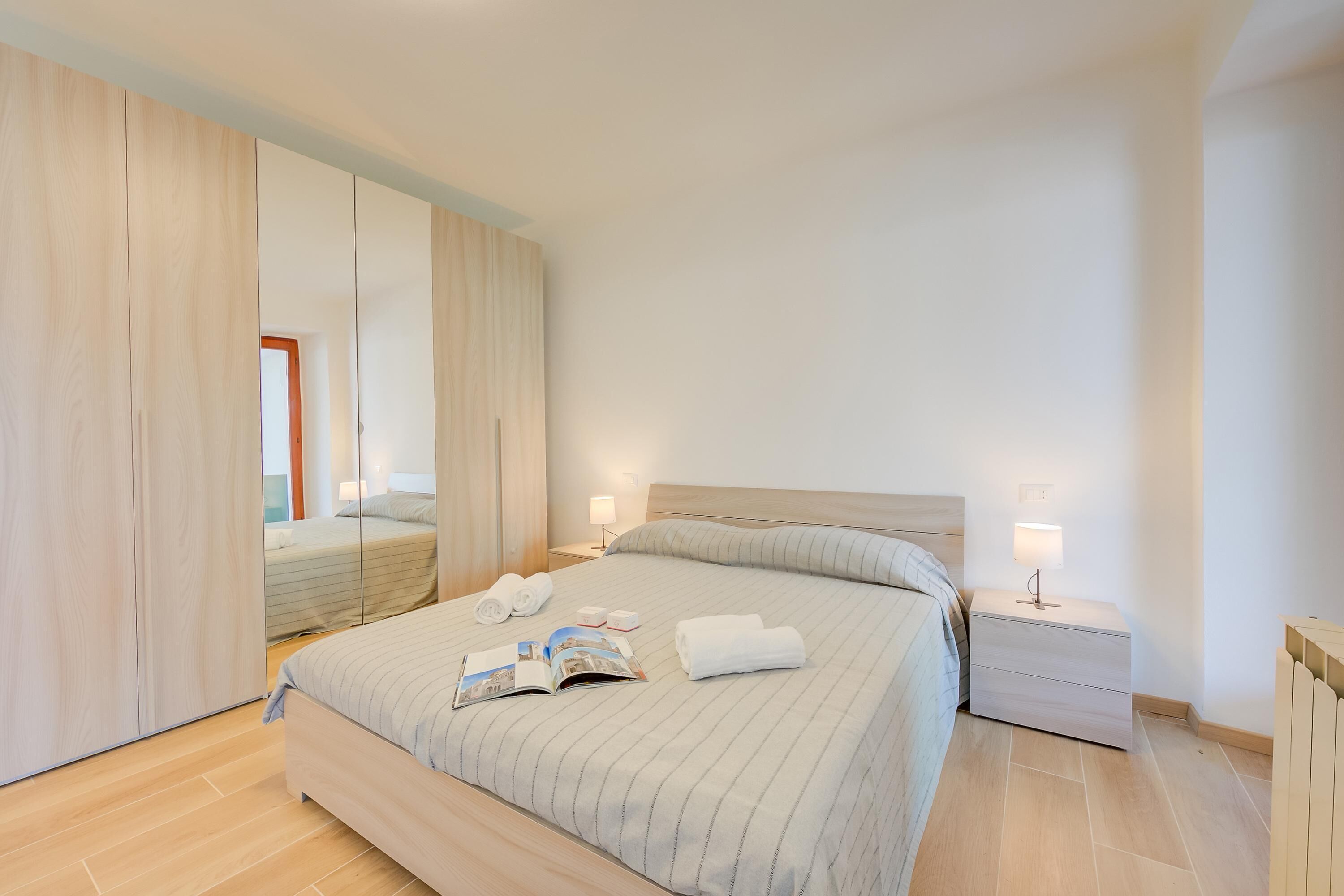 A modern bedroom with a large bed, bedside tables, a mirror, and a wardrobe.