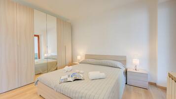 A modern bedroom with a large bed, bedside tables, a mirror, and a wardrobe.