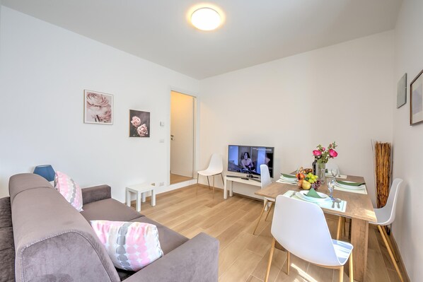 A modern living room with a sofa, a dining table with chairs, a TV, and a small white table. - Red House Terrace Private Beach (Baveno)