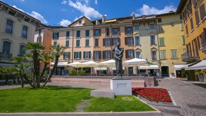 A courtyard with a statue, cobblestone pavement, and buildings with balconies and awnings. - Residenza Faust-historical Center Sal (Salò)