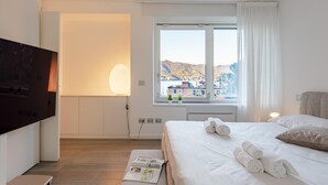 Ett hotellrum med en säng, en tv, ett fönster med utsikt över byggnader och ett nattduksbord med handdukar.