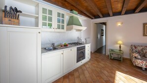 Eine Küche mit weißen Schränken, einem Gasherd und einer Spüle. Die Decke ist aus Holz und oberhalb des Herdes befindet sich ein grüner Schrank.