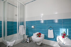 A bathroom with a glass shower enclosure, a toilet with a rose arrangement, and a sink with a mirror. - Villa Mimosa Appartamento 5 (Desenzano del Garda)