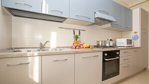Una cocina moderna con gabinetes de colores claros, un lavamanos de acero inoxidable, un microondas y una estufa a gas.