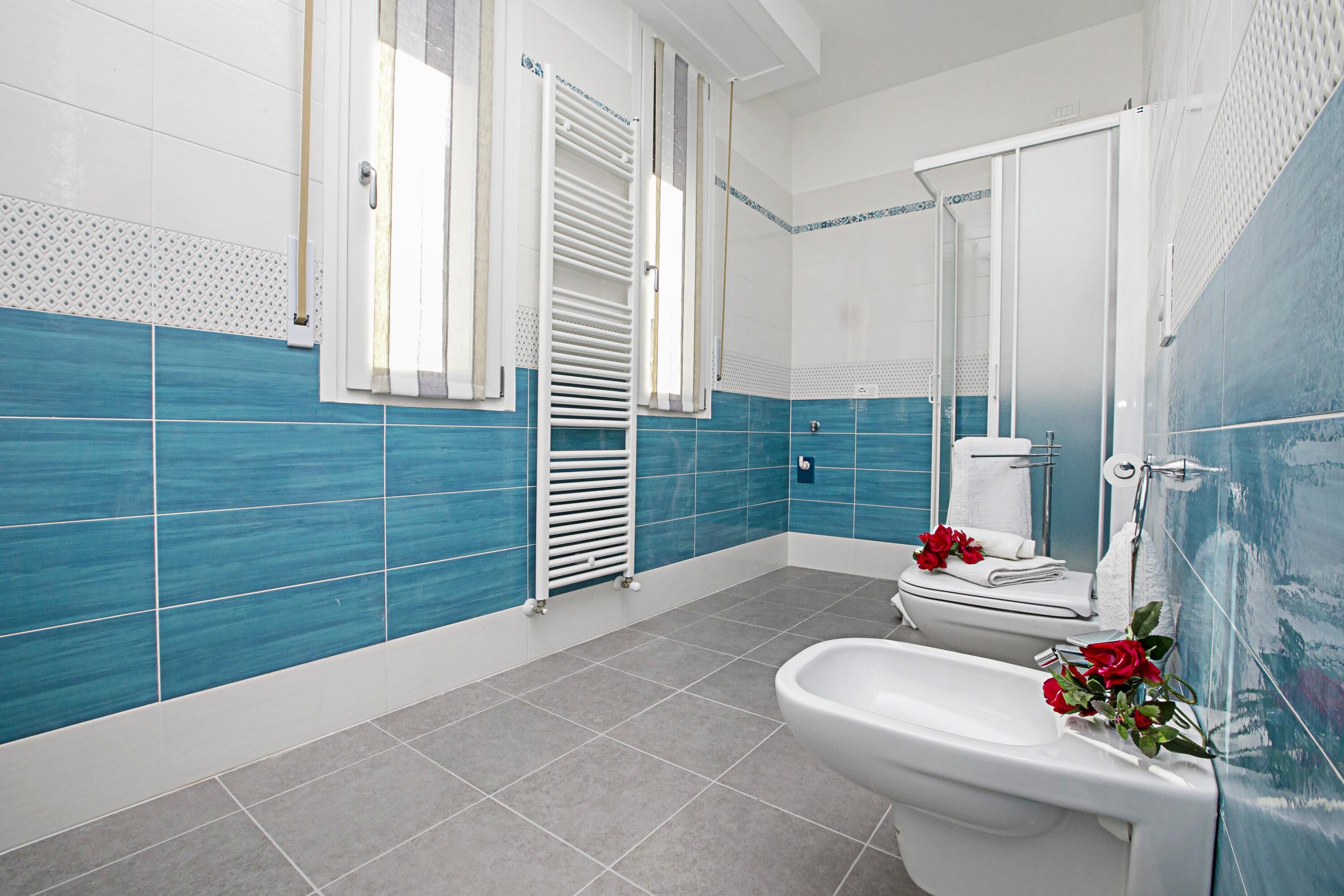 A bathroom with blue and white tiles, a white toilet, a bidet, and a shower area.