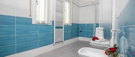 A bathroom with blue and white tiles, a white toilet, a bidet, and a shower area.
