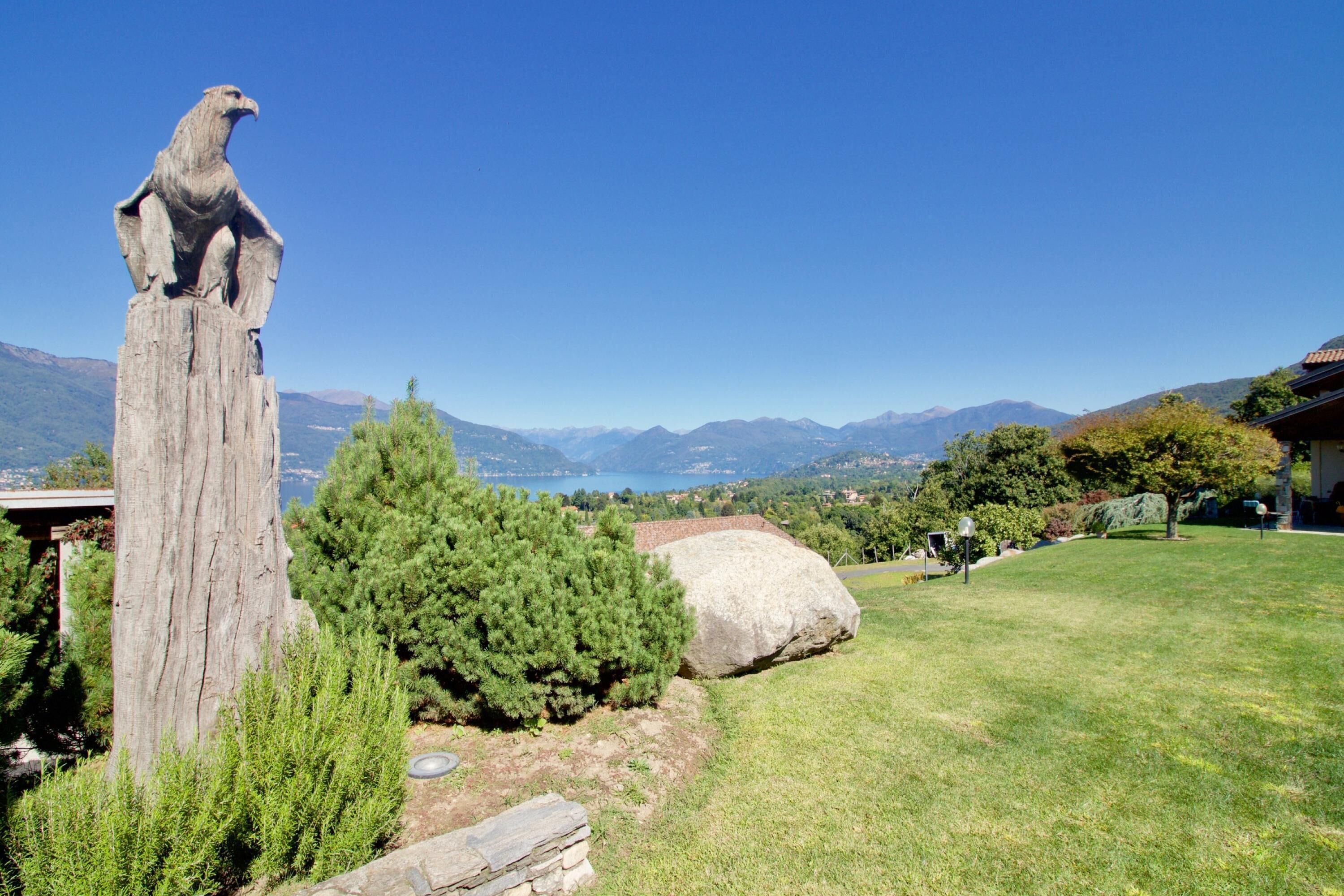 A wooden sculpture of an animal on a post, a large rock, and a grassy area with trees and mountains in the background.