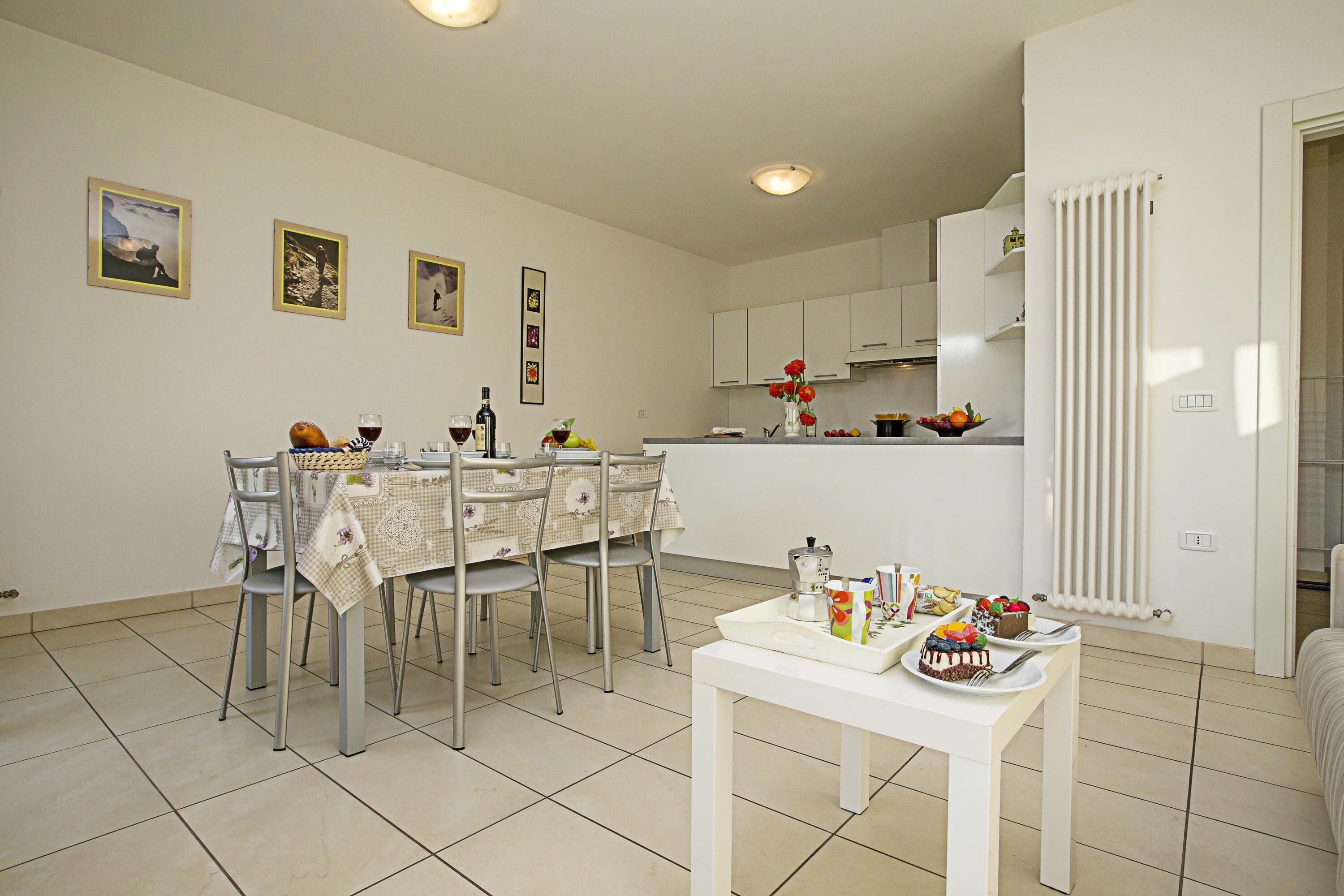 A modern kitchen with white cabinets, a dining table with chairs, and a small white table with food and drinks.