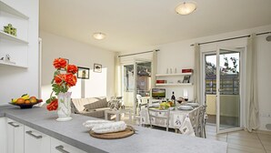 A modern kitchen with a marble countertop, a dining area with a table set for four, and a view of the outside through a sliding glass door. - Torbole Relax Pool Balcony Apartment (Nago-Torbole)